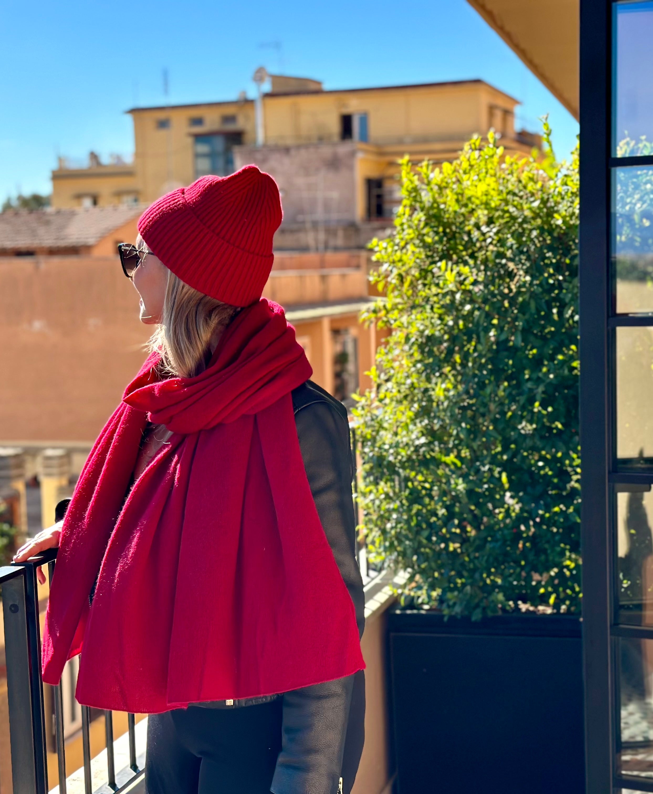 SAINTE MER Gründerin Marlen trägt leuchtend roten Kaschmirschal und -mütze auf einem Balkon in Rom – stilvolle Eleganz und Wärme für urbane Wintertage.